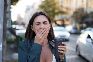 Caucasian woman with cup of coffee outdoor city street yawning sleepless tired