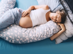 Pregnant woman relaxing or sleeping with belly support pillow in bed. Pregnancy concept.