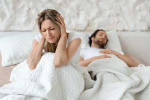 Unhappy angry woman sitting on bed and covering her ears with hands, suffering from her husband